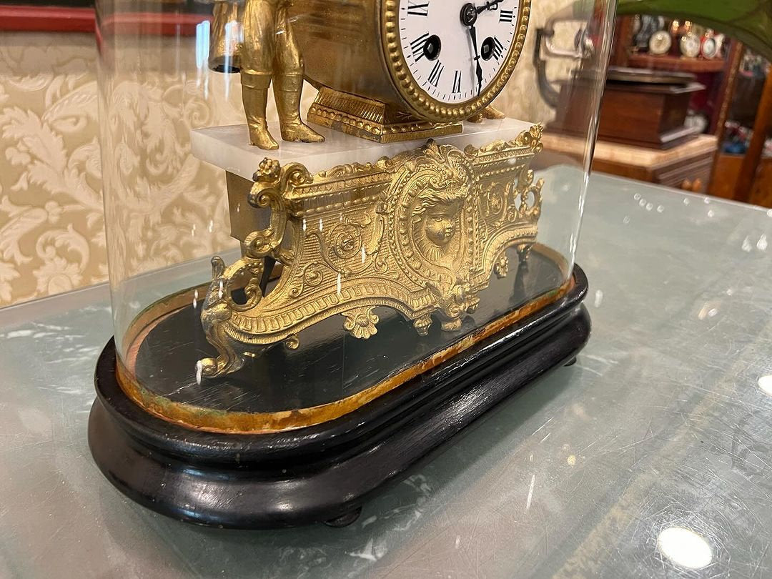 Antique French 1890s glass-domed marquetry fireplace clock with intricate gold detailing and wooden base on display